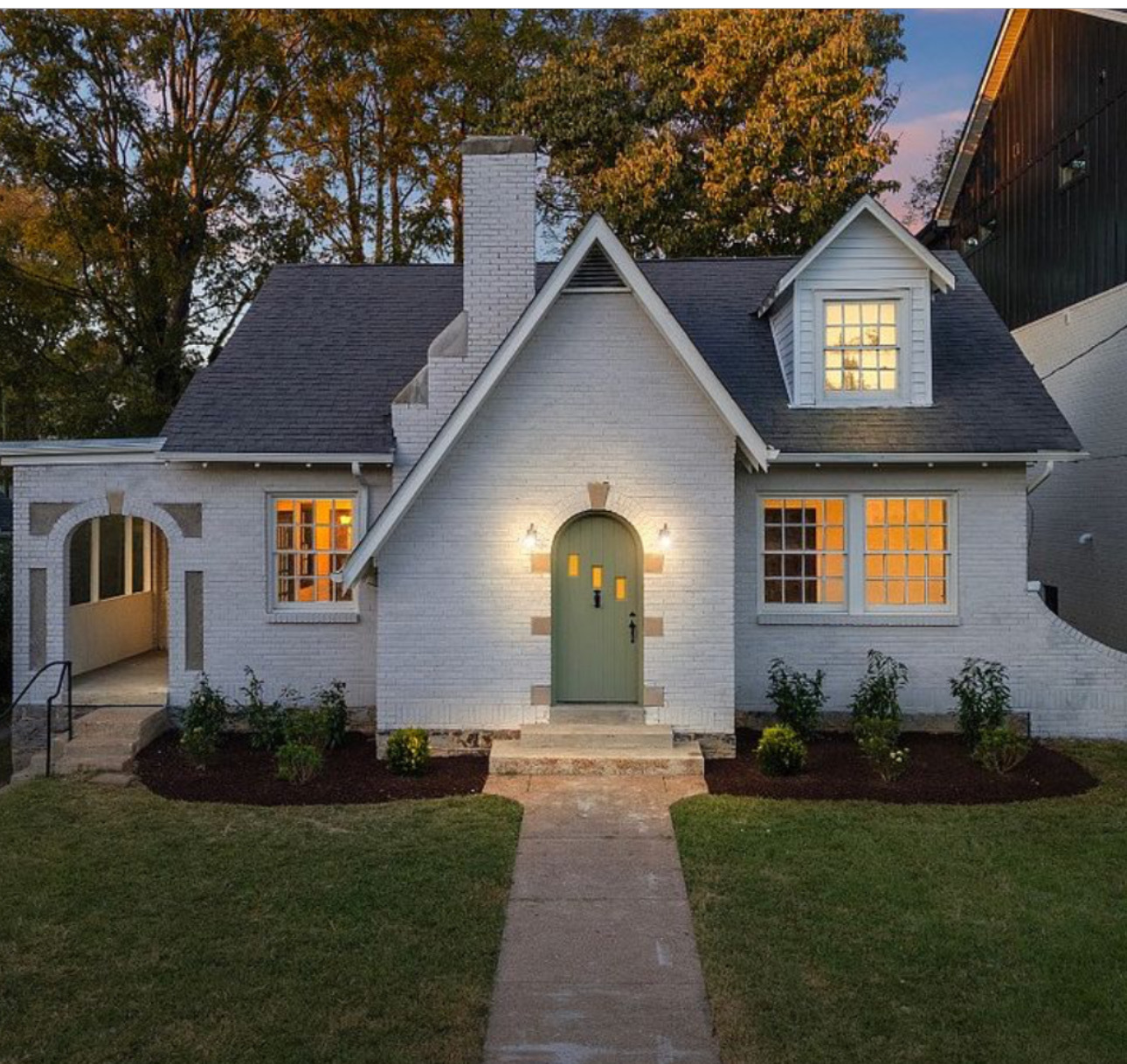 Renovated Nashville cottage at dusk with warm interior lighting glowing through the windows